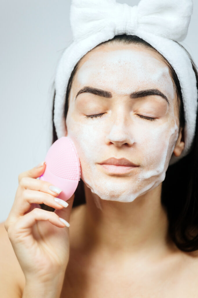 woman using electric cleansing brush for face deep cleaning . Beautiful woman clean face with cleansing brush.