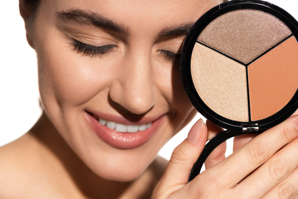 close up view of happy young woman holding bronzer and highlighter palette isolated on white. face highlighters