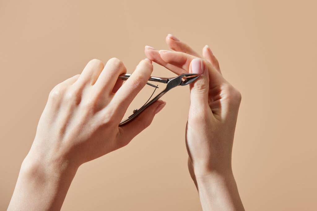 Cropped view of woman doing manicure with cuticle nipper isolated on beige. cuticle nipper. nail cutting tools