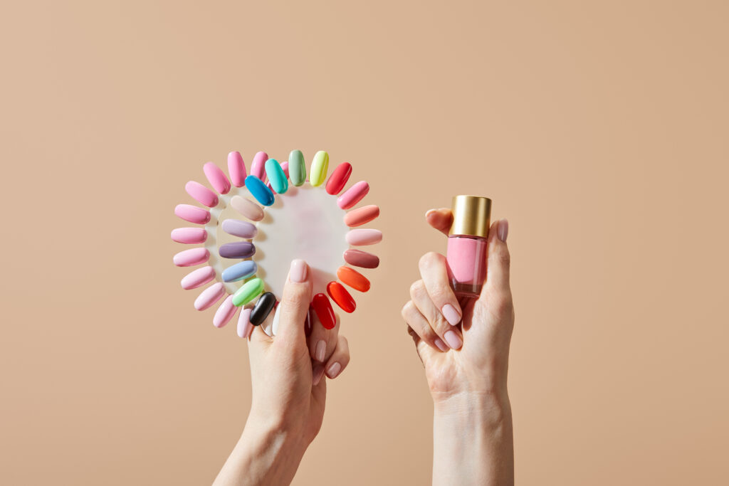 Cropped view of woman holding bottle and samples of nail polish isolated on beige. 2024 nail polish color trends. 2024 nail polish shades. Summer, Spring, Fall and Winter nail polish shades.