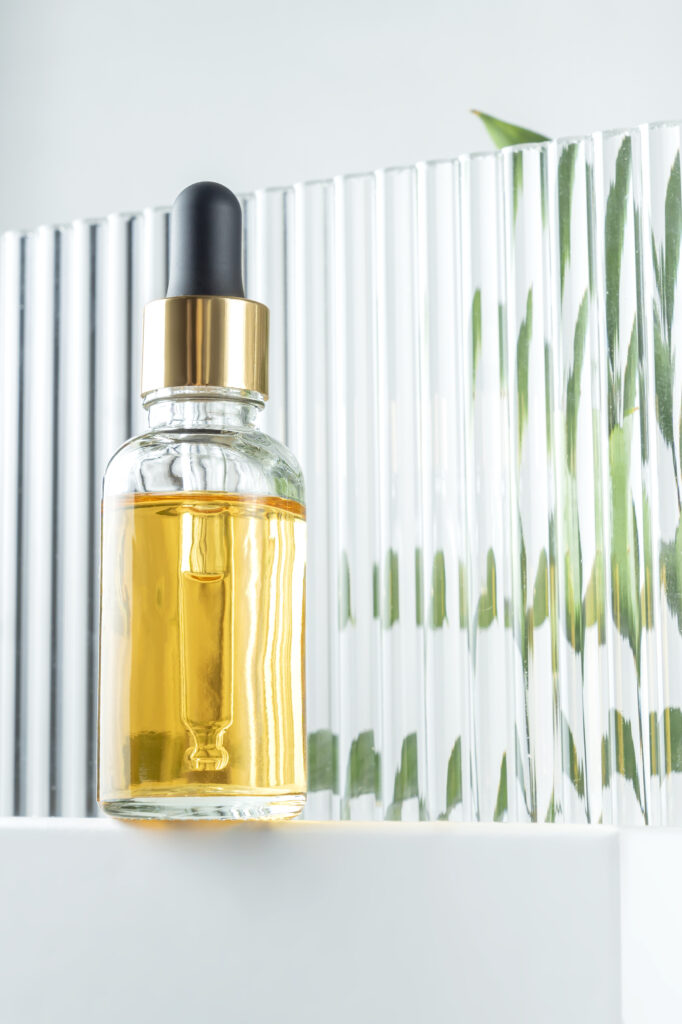 Hair Serum bottle. glass cosmetic bottle with a dropper on a plexiglass background with tropical leaves. Natural cosmetics concept, natural essential oil and skin care products