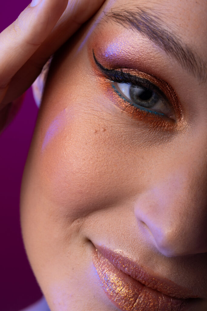 Portrait of caucasian woman wearing golden eye shadow and lipstick on purple background. Cosmetics, makeup, female fashion and beauty, unaltered.