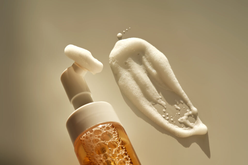 Beige facial foam with a dispenser and brush in the rays of the setting sun. High quality photo.