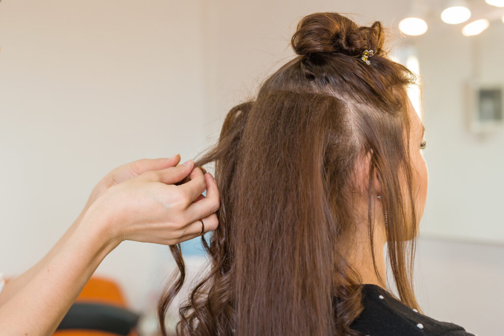 Closeup hairdresser coiffeur makes hairstyle for young woman. Curly hair. DIY curly hair.