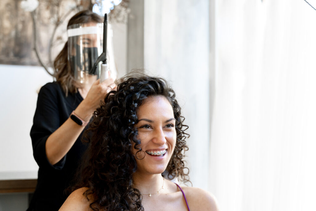 Hairdresser with a plastic protection facial mask and a client in a hairdresser salon after doing perm hair.