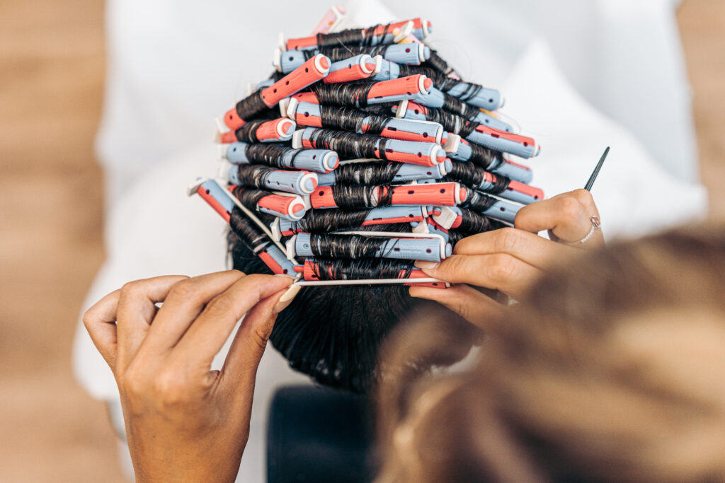 Aerial photo of the hands of a hairdresser fixing the hair of a man with curlers in a salon. DIY perm hair.