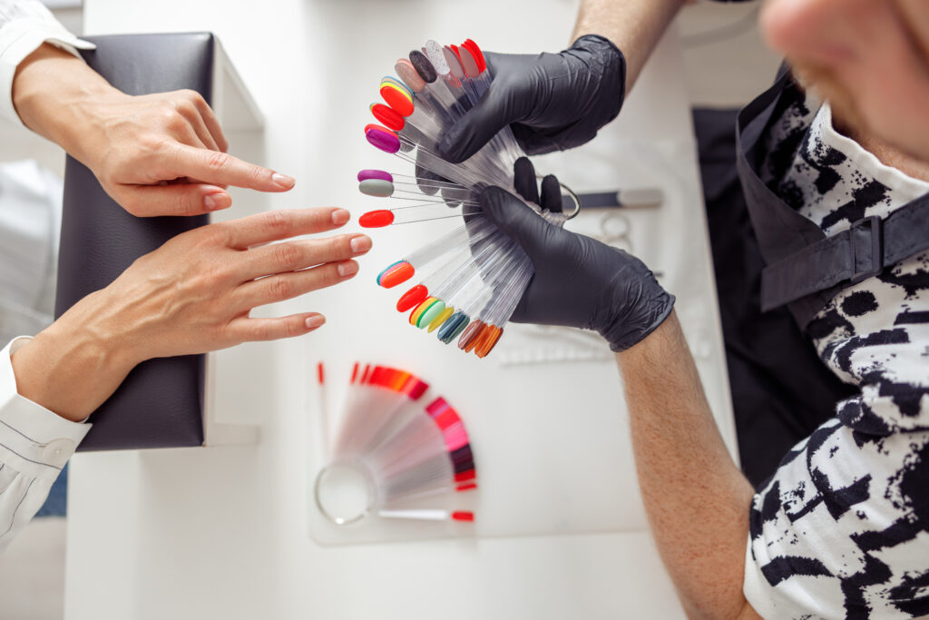 Top view of man nail technician showing color samples of nail polish to female client in beauty salon. nail polish for fair skin