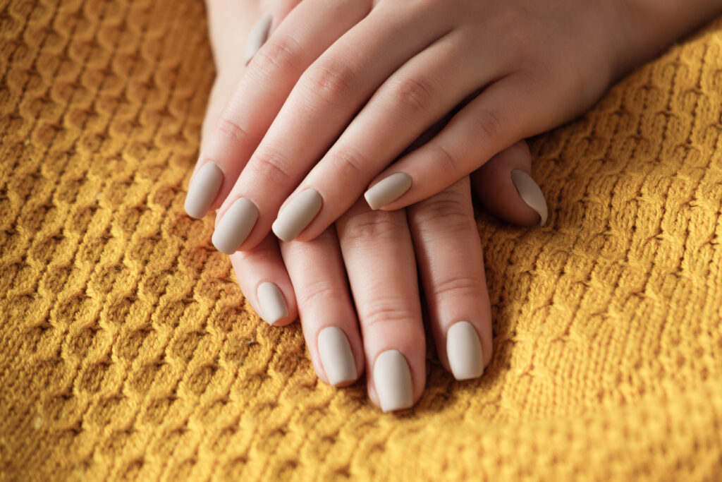 Chocolate Milk Nails. Matt nude beige nails close up. Winter or autumn manicure, woman hand on the warm yellow sweater.