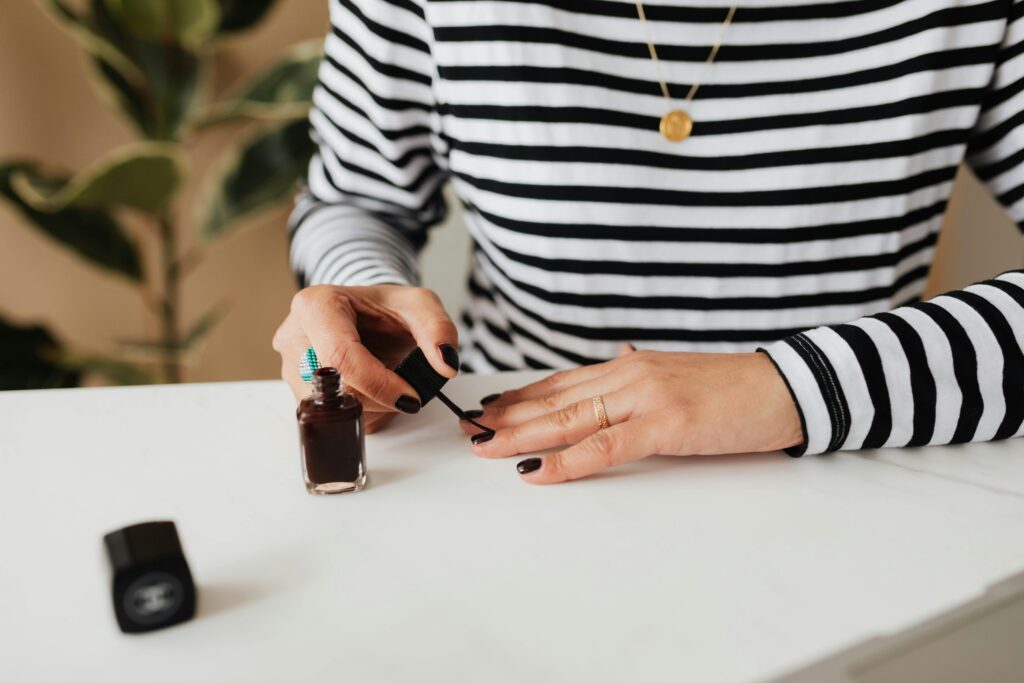 A faceless woman applying brown nail lacquer shade on her nails