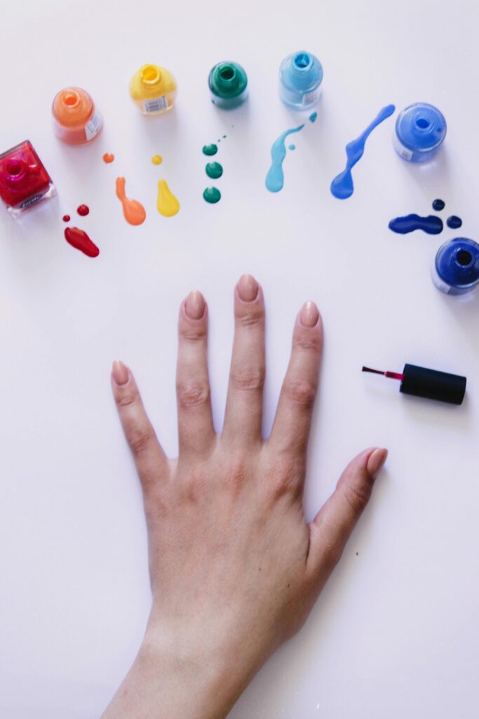 Opened nail polish bottles in different colors with a faceless woman nails painted in nude nail polish color