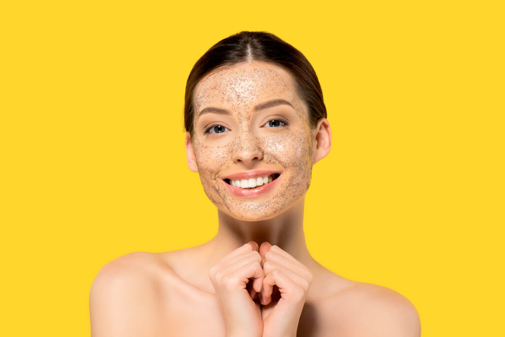 portrait of cheerful naked girl with peeling mask, isolated on yellow. face wash cleansers