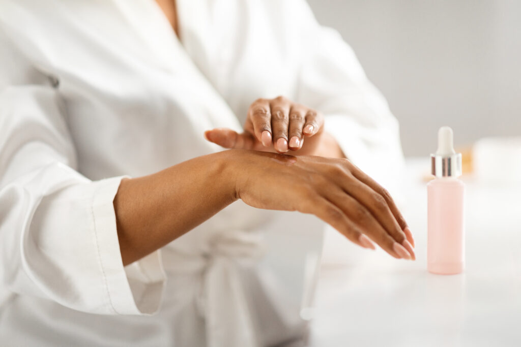 Skin Moisturizing. Black Woman Applying Nourishing Serum On Hands At Home, Closeup Shot Of Unrecognizable African American Female Testing New Beauty Product While Making Beauty Routine. Hand and feet care