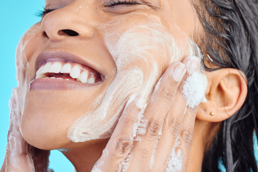 Studio shot of a young woman washing her face while taking a shower against a blue background. face wash cleansers