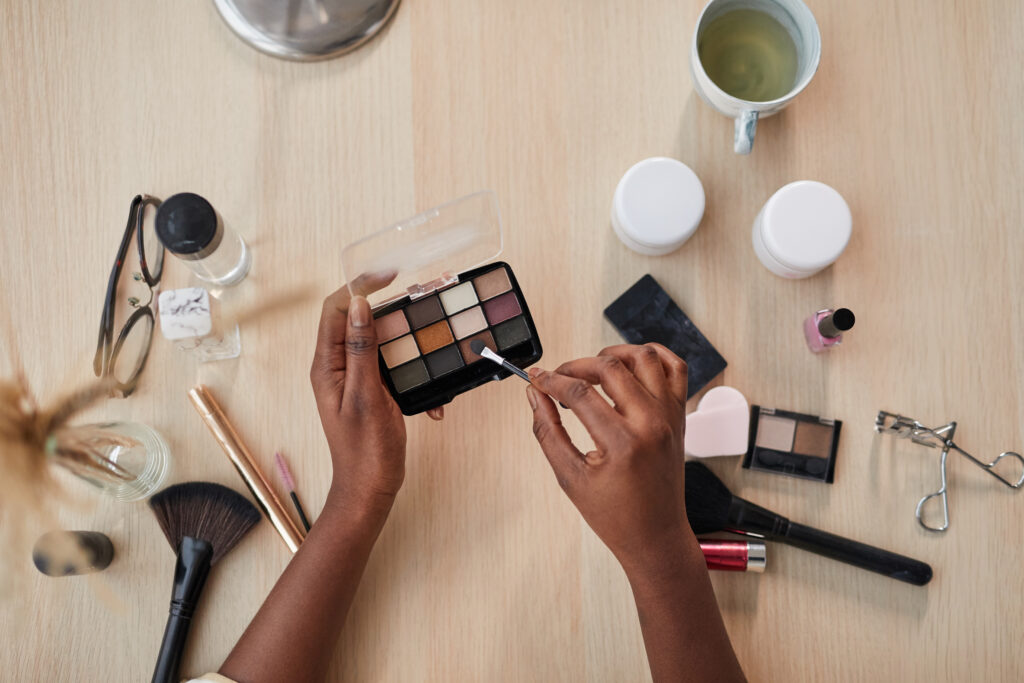 Top view closeup of female hands holding eyeshadow pallete over table with various beauty products while doing makeup. eyebrow hues