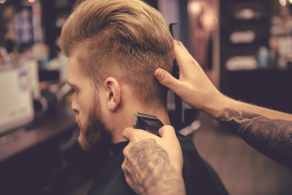 Back view of handsome bearded man getting haircut by hairdresser at the barbershop. hair trimmers. home hair cut. DIY hair cut