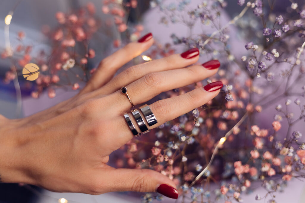 Close shot of  woman hand fingers wearing two rings, bouquet  of colorful dried flowers, pink purple colors, shiny bright warm lights. manicure. painted nails. colored nails