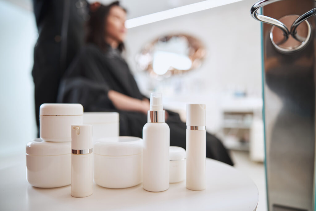 Blurred photo of a dark-haired Caucasian woman in a hairdressing cape sitting in the barber chair during the hairstyling procedure. hair masks