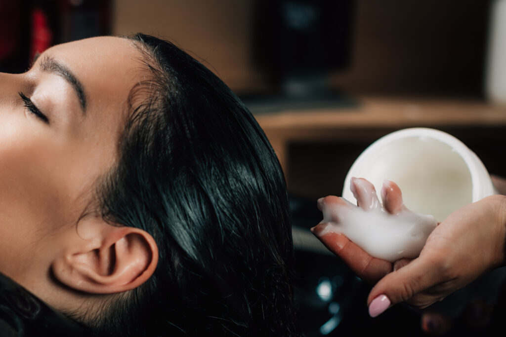 Beautiful woman in hairdresser’s salon. Hairstylist applying conditioner on woman’s hair. Key Ingredients to Look For in a Hair Mask