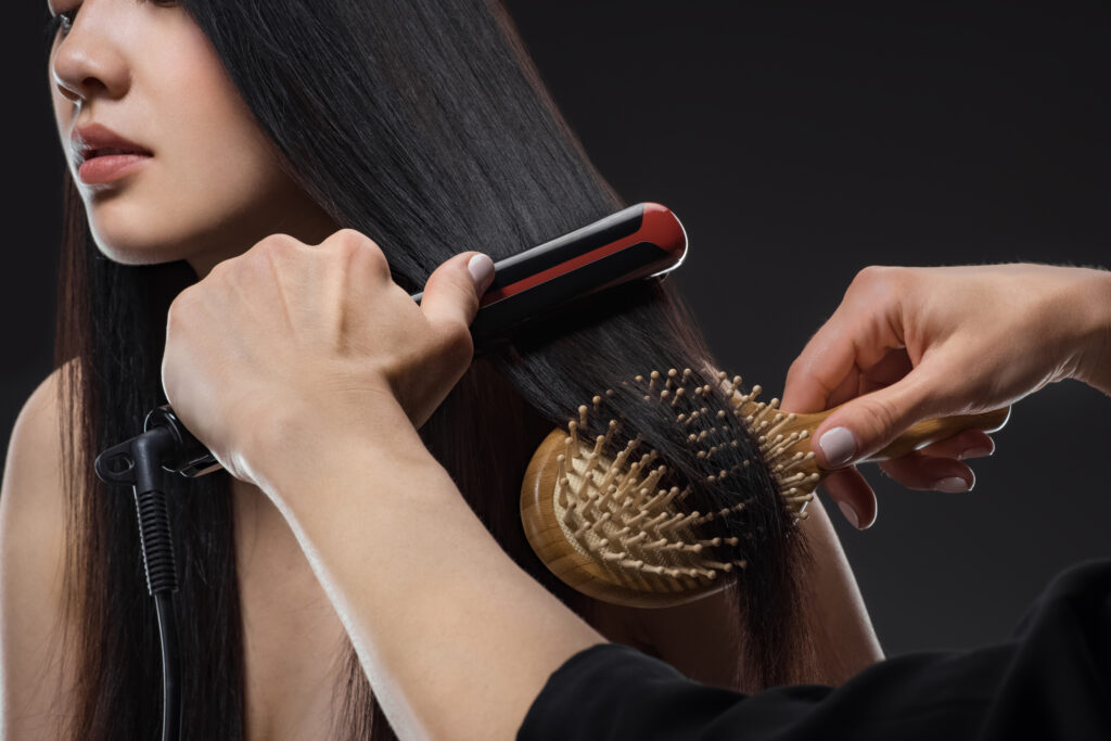 partial view of hair stylist straightening womans hair with hair straightener and brush isolated on. hair brushes. hair brush