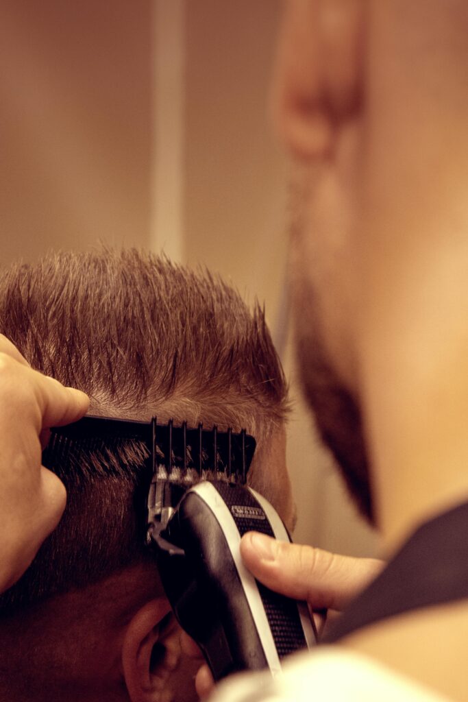 A stylist is using hair trimmers to cut a client's hair. DIY hair cut. 