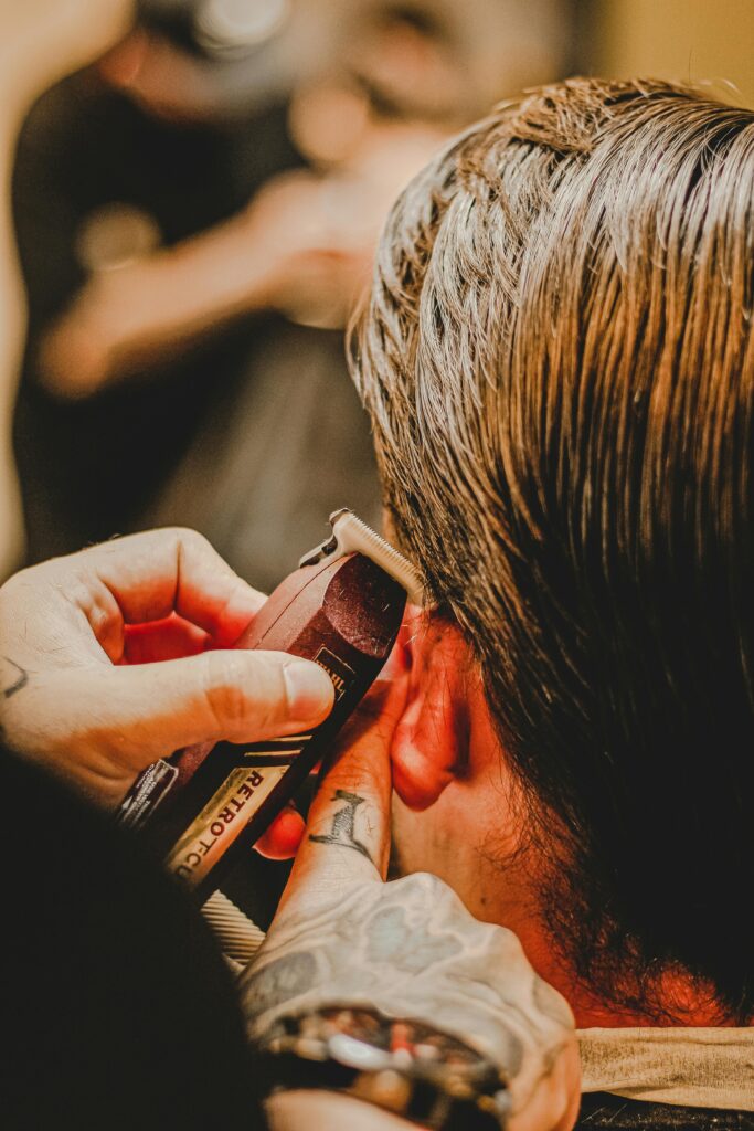 A faceless stylist is using a hair trimmer to cut a client's hair.