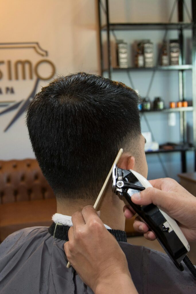 A man is getting his hair cut by a stylist using a hair trimmer in a salon.