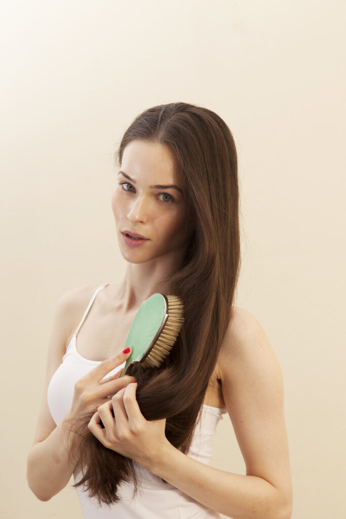 Boar Bristle Brushes. Portrait of young woman brushing hair, looking at camera