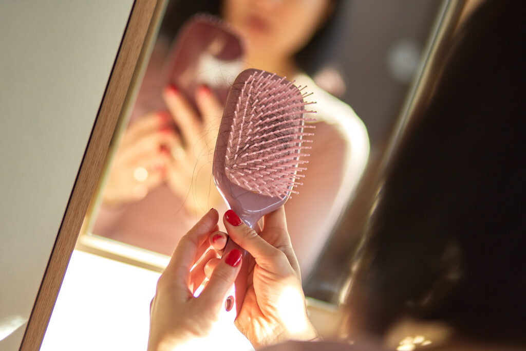 Paddle Brushes. Problem hair loss concept, losing hair on hairbrush, Pretty Brunette woman brushing hair with comb in front of the mirror at the morning at home, sunlight,