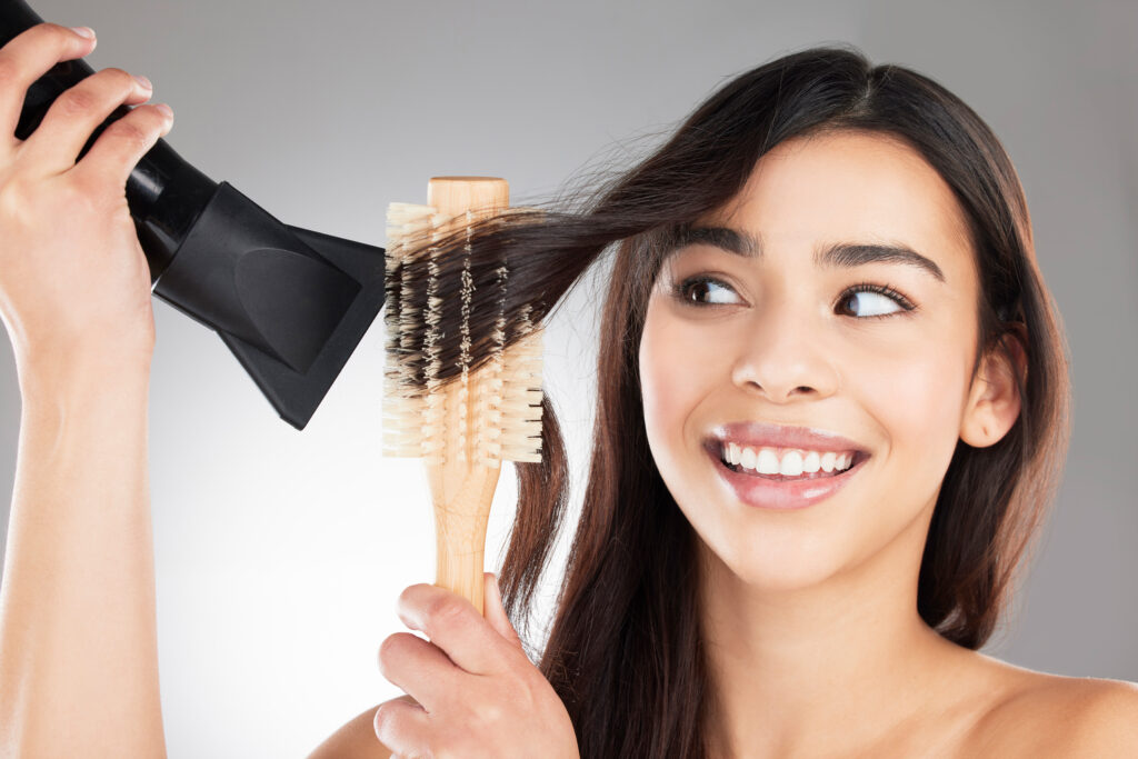 Common Mistakes to Avoid when using hair brushes. Studio shot of a beautiful young woman styling her hair against a grey background.