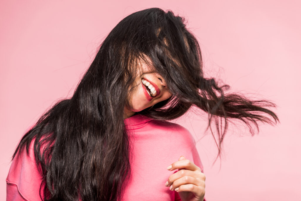 woman in pink pullover smiling and playing with hair isolated on pink