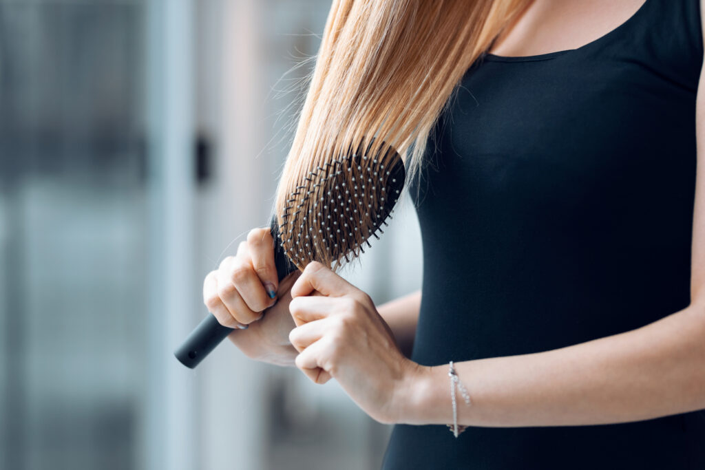 Features to Look For in the hair brush. Close up of young attractive woman brushing her long blonde hair at home.