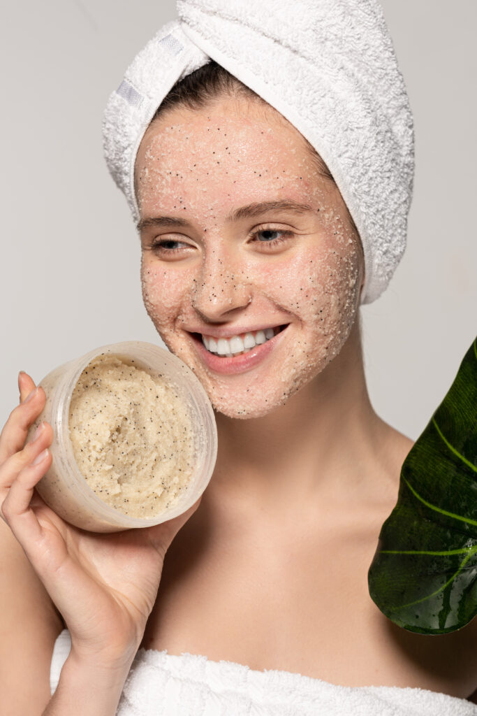 cheerful woman with towel on head holding green leaf and plastic container with coconut scrub, Facial scrub. face caring. skin care.