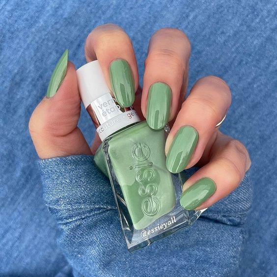 A faceless woman holding an Essie Gel Couture bottle in a green shade.