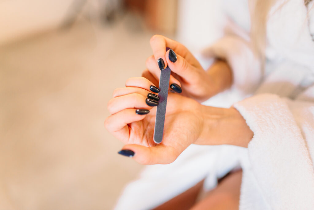 A faceless woman with bold blue painted nails is filling her nails at home. At-home manicure. 