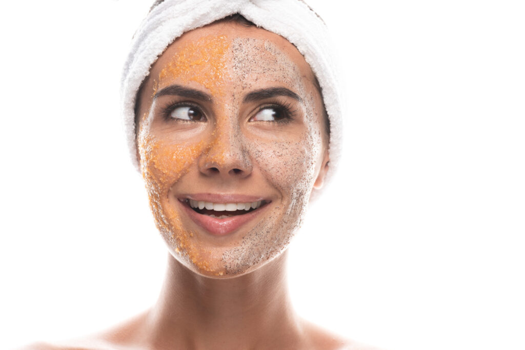 front view of excited young woman in cosmetic hair band with scrub on face isolated on white.