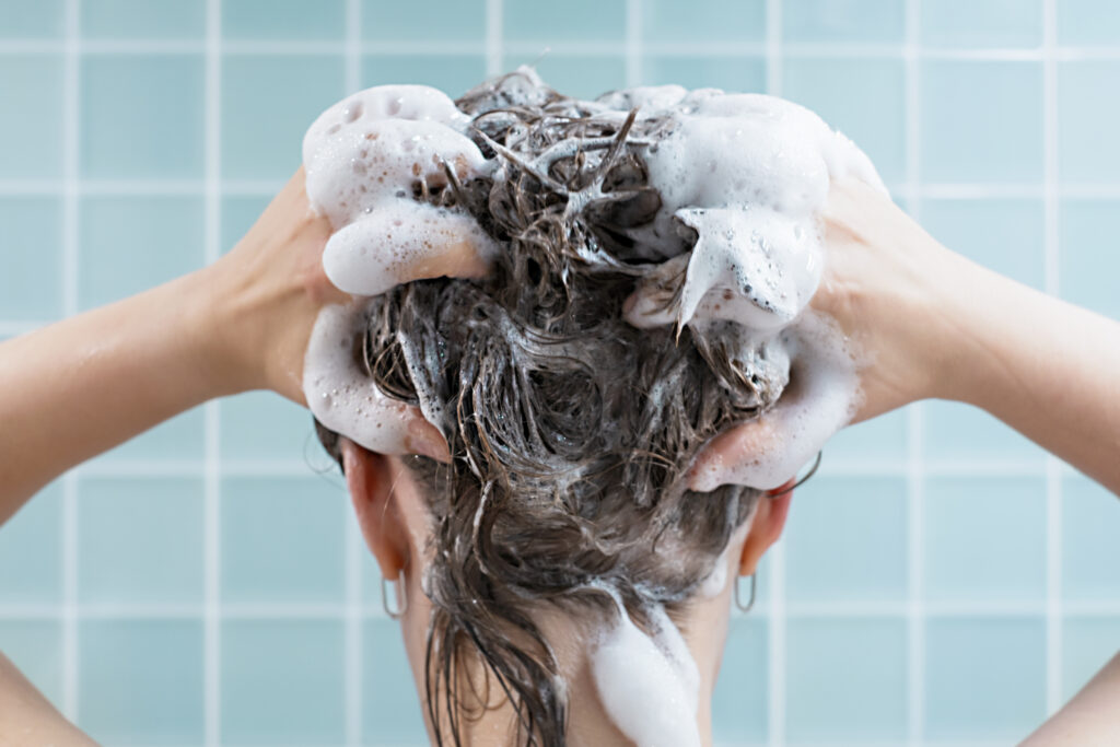 Girl washes her hair with shampoo on a blue background, back view. Hair care. Hair treatments. DIY hair care.