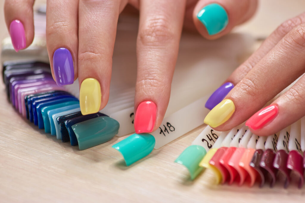 Manicured fingers touching nails samples. Female fingers with bright summer manicure and nails samples. Variety of nails colors in beauty art salon. Gel polish shades. Nail polish shades.