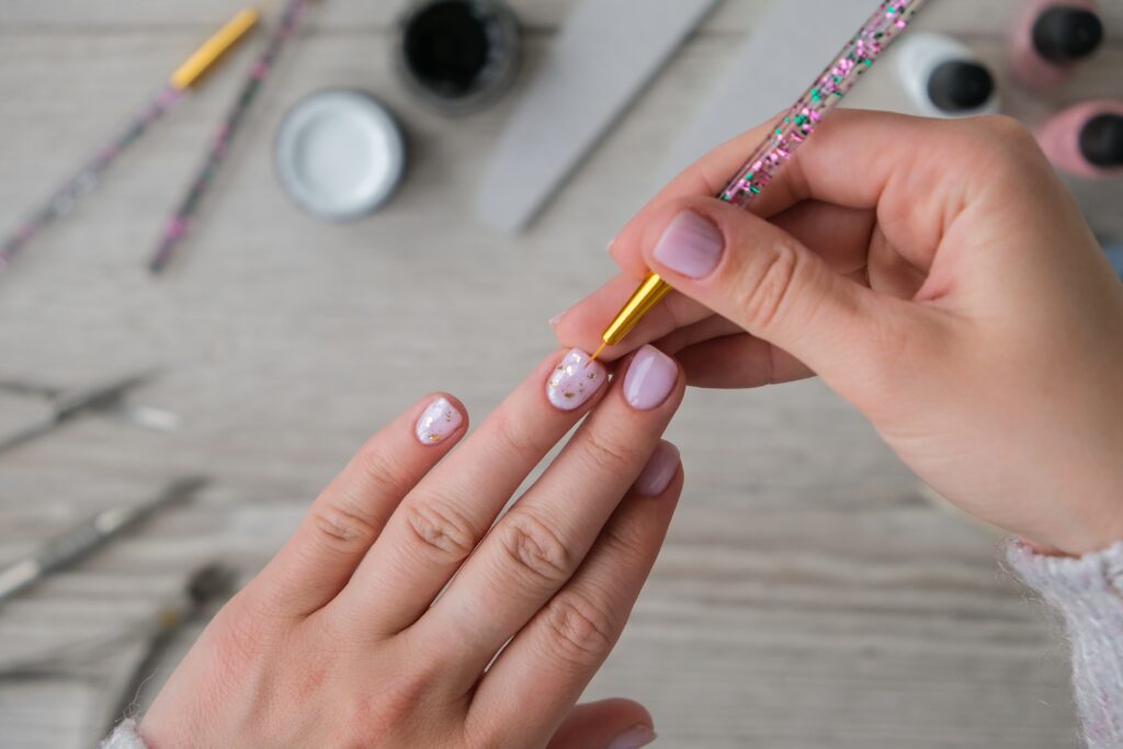 A faceless female applying gold nail designs on her pink painted nails at home.