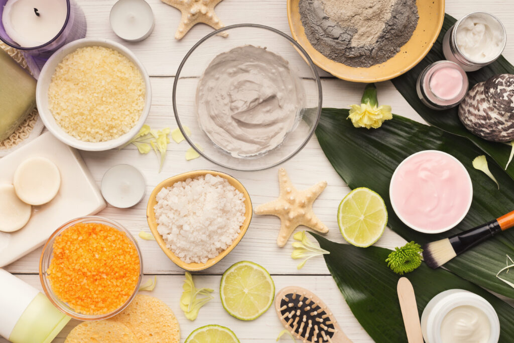 Cosmetology mud mask and natural spa product on white wooden background with green leaves. Skincare concept, top view.