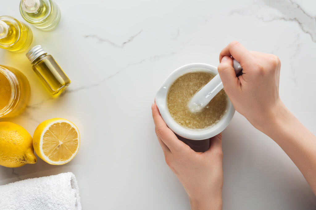 partial view of woman making salt and oil scrub in pounder on white surface.