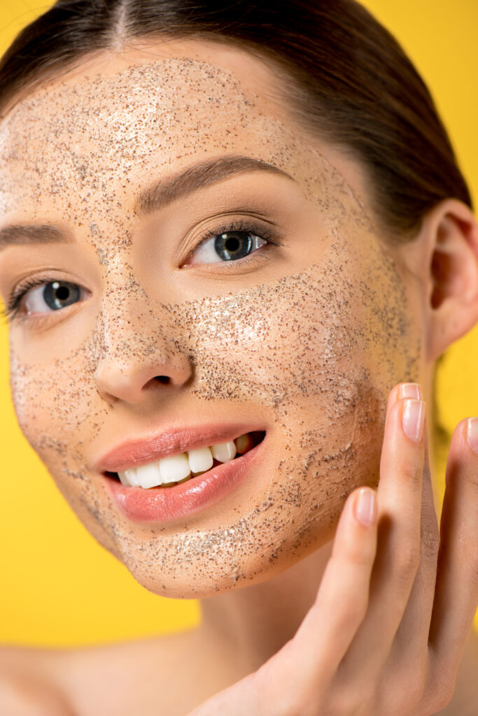 portrait of happy young woman applying peeling mask, isolated on yellow. facial scrub. facial care. face caring.