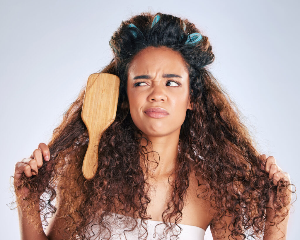 A woman is frustrated with her dry hair, with a hairbrush stuck in her tangled locks.