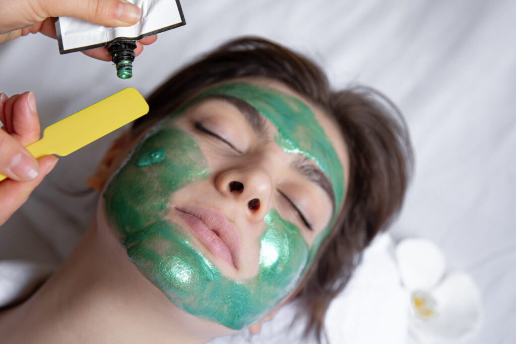 The process of applying a green cosmetic mask to the face of a young woman, spa procedure in the salon, beauty and skin care.