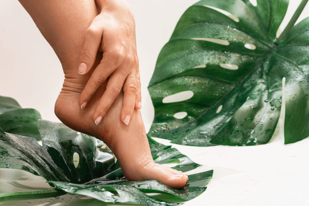 Closeup of wet female feet with smooth skin and Monstera deliciosa tropical leaf