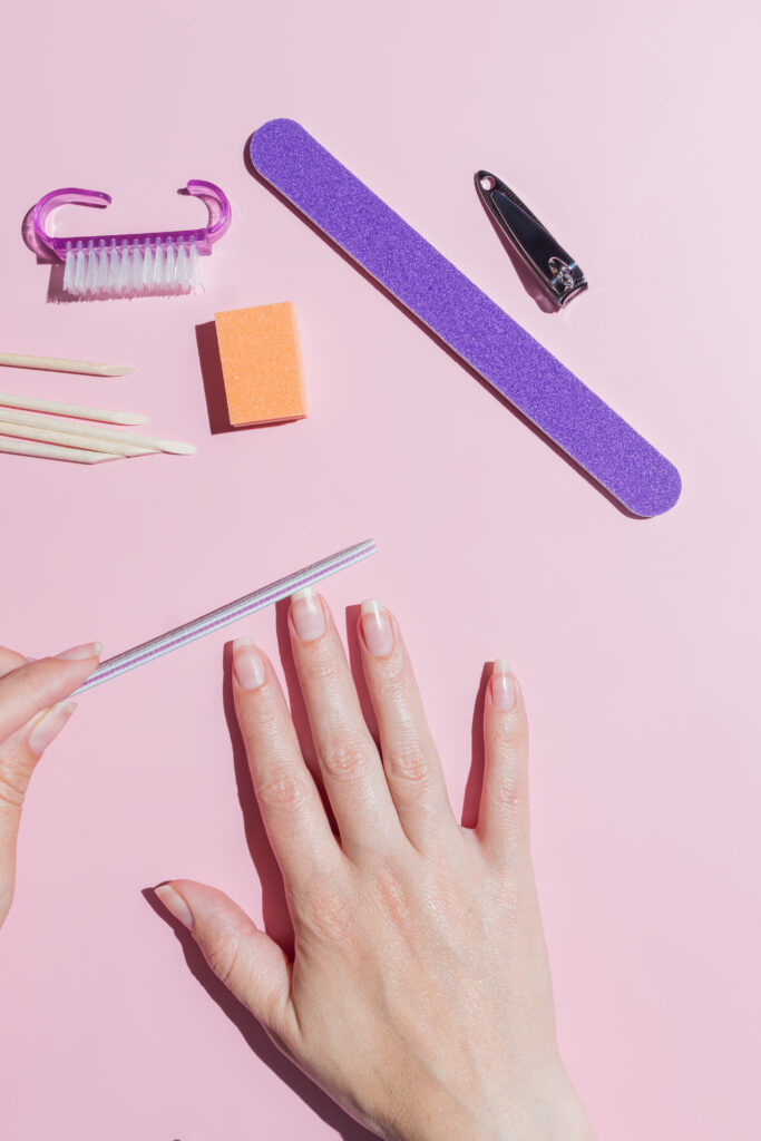 Woman aligns her nails with a nail file. Alignment of the nail edge. Manicure at home for yourself. A woman's hand with healthy natural nails. procedure of nail care. Top view. Nail tools. nail care. Nail products. Home nail care. DIY nail care.