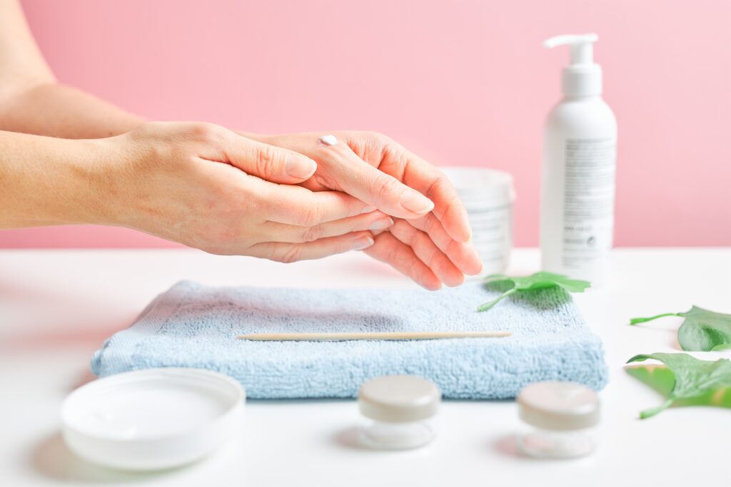 Woman applying  cosmetic moisturizing hand cream. Cosmetic products, green leaves on white table. Spa, manicure, skin care concept. Flat lay, overhead view. skin care. hand care.