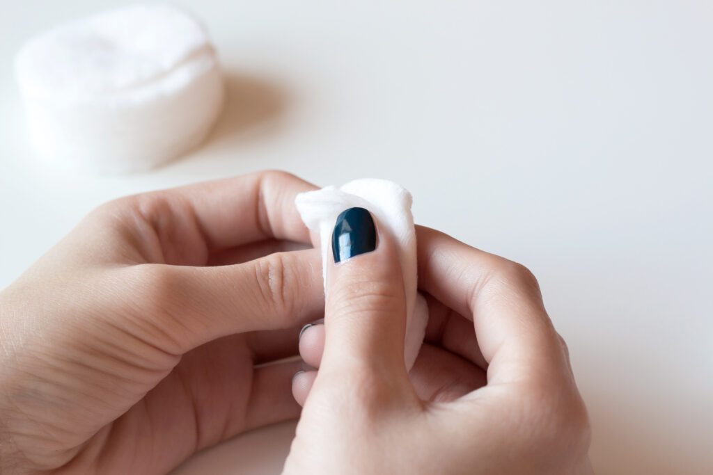 Woman removes the nail polish with cotton wheels. Hands with dark blue manicure on whote table.