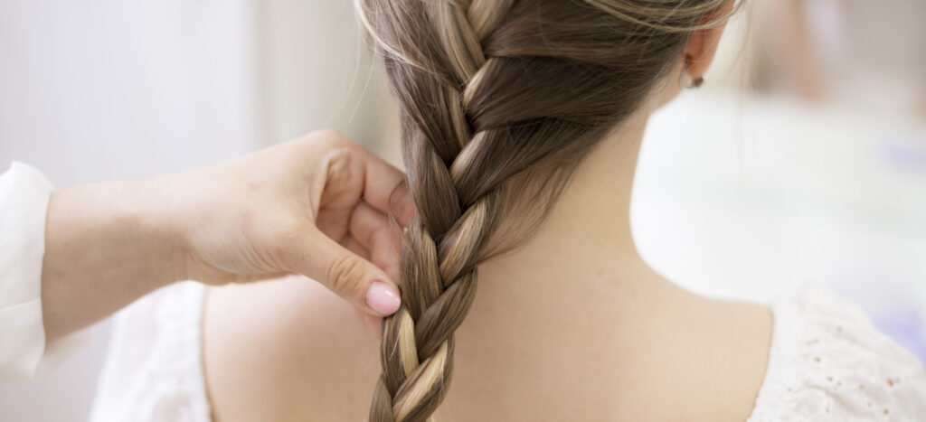 hairdresser making a braid to a young fashion model, backstage preparation. Braided Ponytail. 