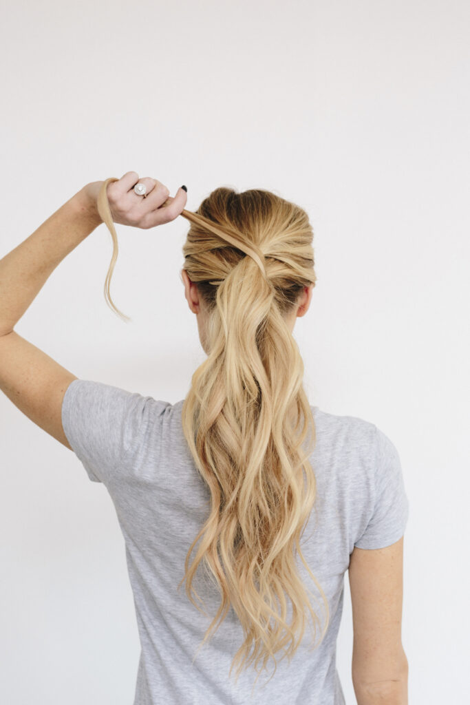 ways to style quickly on busy mornings. a young woman with long blond wavy hair. Tying a ponytail. Back view. Everyday Hair Styling