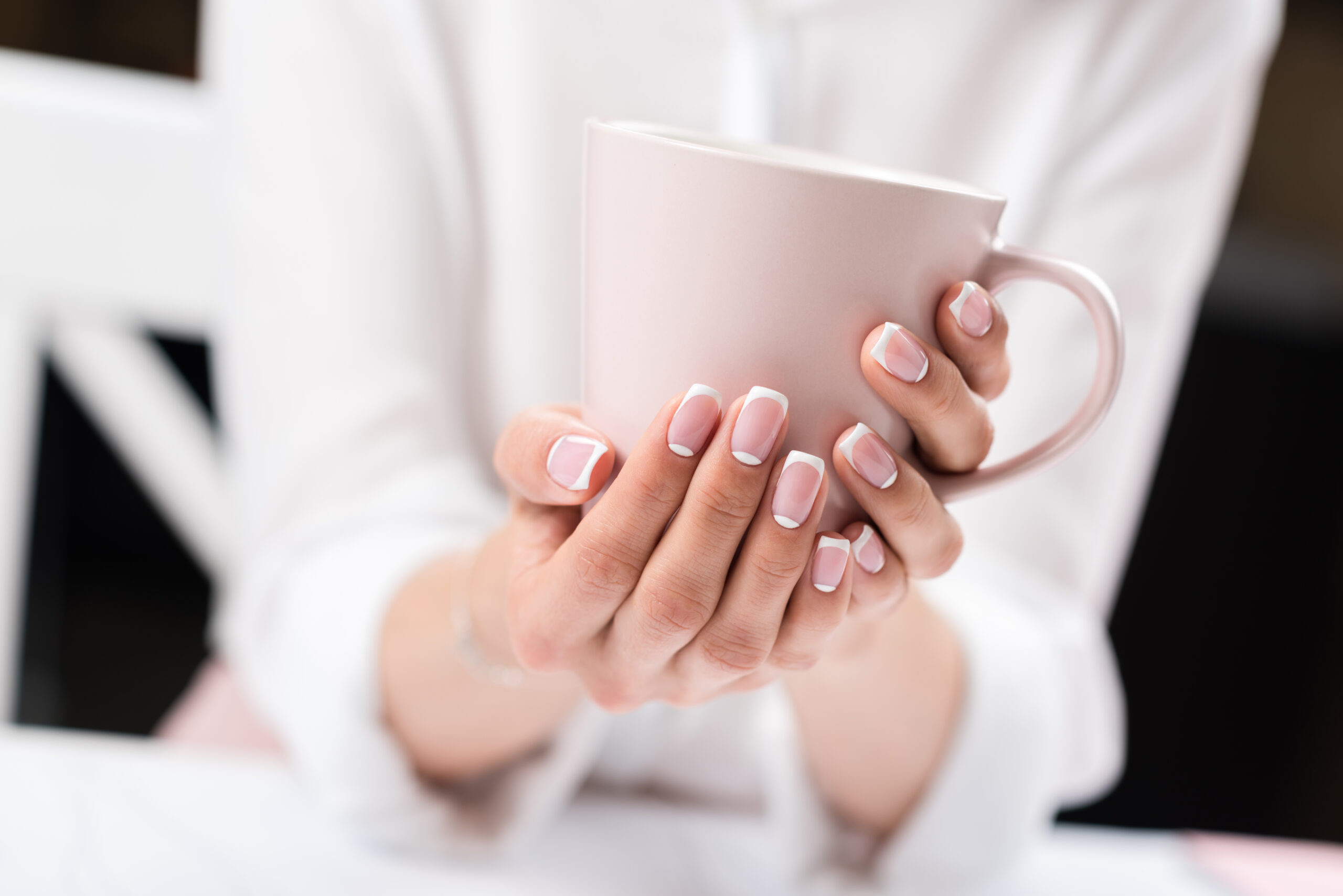 close-up partial view of young woman with beautiful manicure holding cup of coffee. french manicure using OPI gel polish